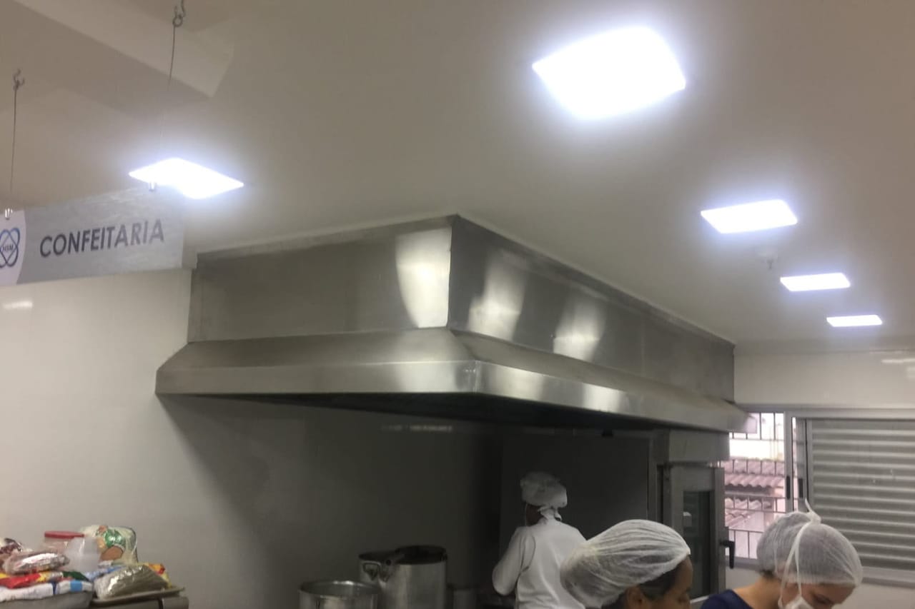 Coifa em aço inox sobre linha de cocção em cozinha industrial em operação